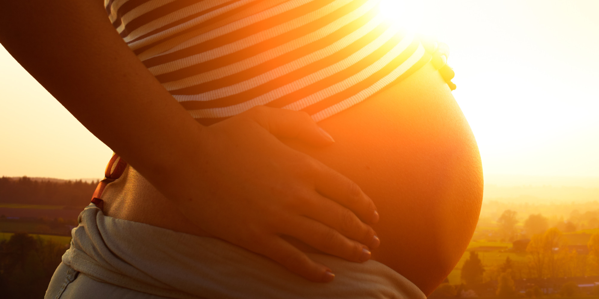 Pregnant woman holding bump at sunset.